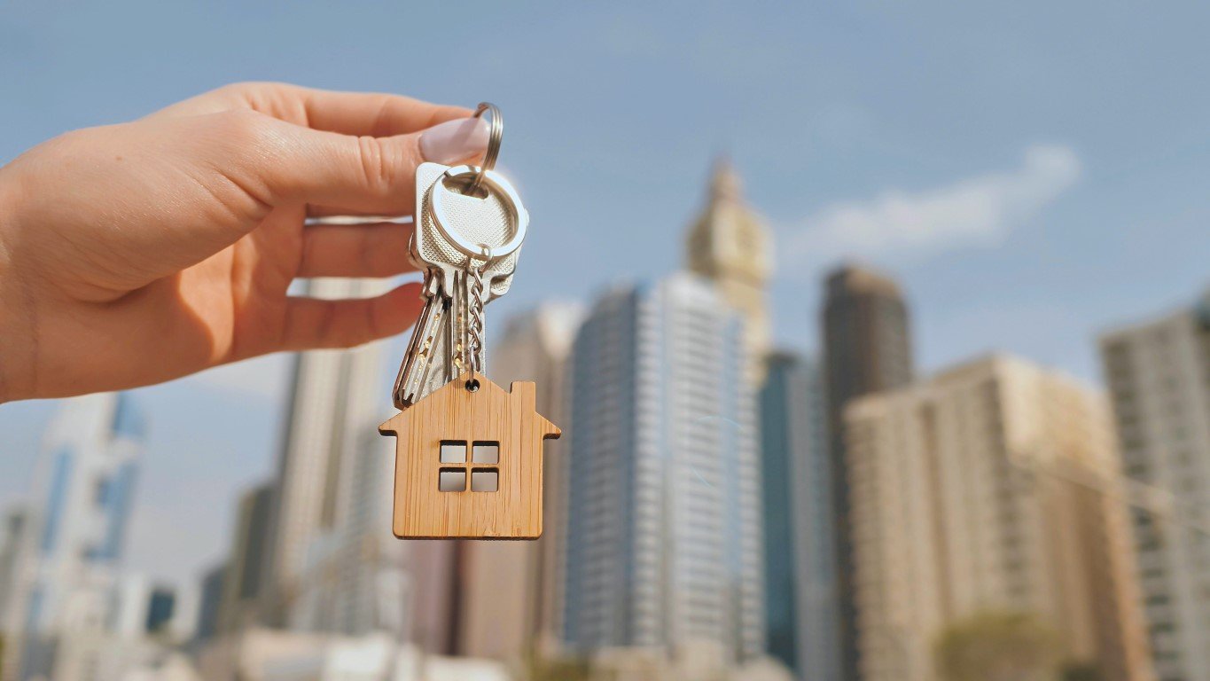 Real estate purchase concept. The girl holds the keys to a new house on the background of a Dubai skyscraper.;AB_Money_2212_46-49_buying property